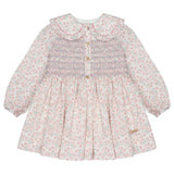 A long-sleeve baby girl's dress with a pink and white floral print, featuring a smocked bodice with gold buttons and a large ruffled Peter Pan collar.